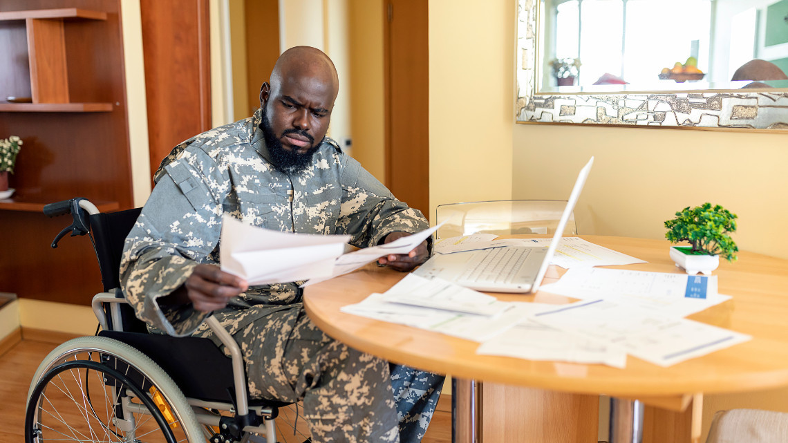 A person in a wheelchair sitting at a table with papers and a laptop