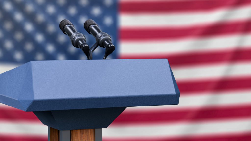 placeholder image of a podium at a debate set against an American flag background