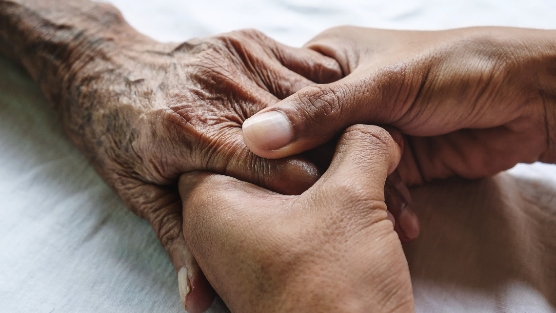 An older hand held by two younger-looking hands