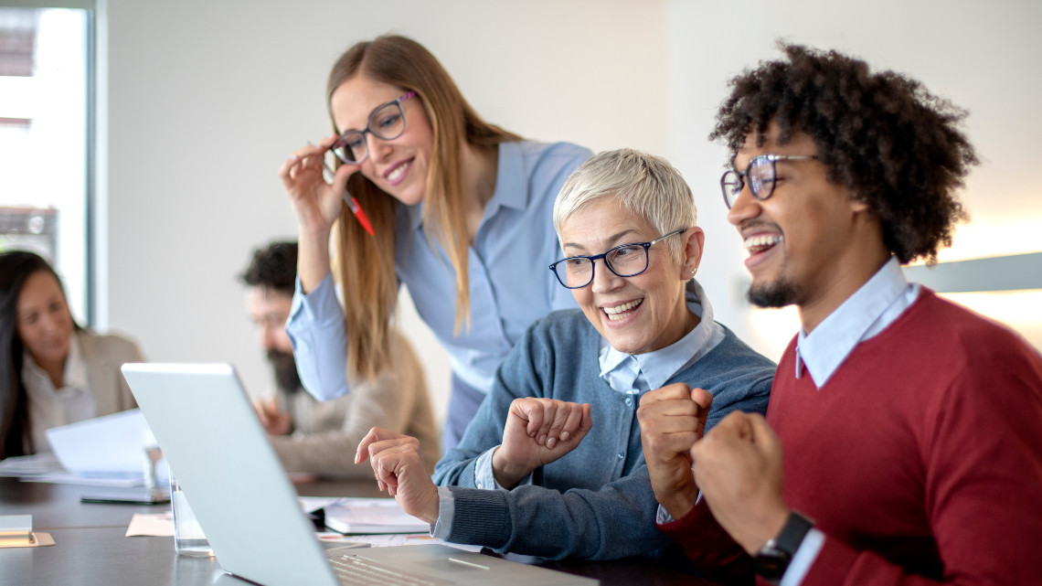 Group of coworkers from different generations excitedly looking at a laptop.