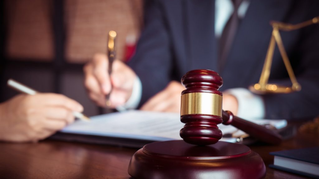 Close-up of a gavel with a gold band on a desk in a legal setting.