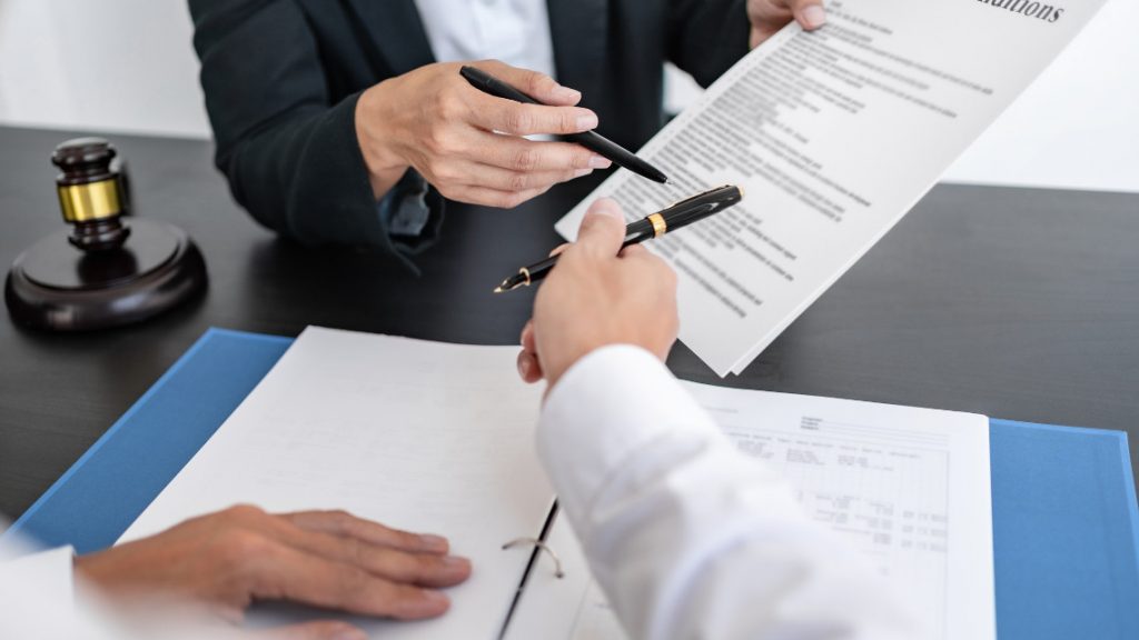 Two people discussing a document at a table, with a gavel nearby. Signifying a small business owner working with a lawyer.