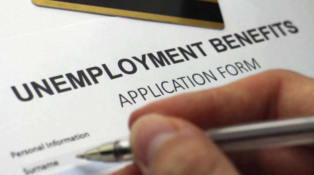 Close-up of an unemployment benefits application form with a hand holding a pen.