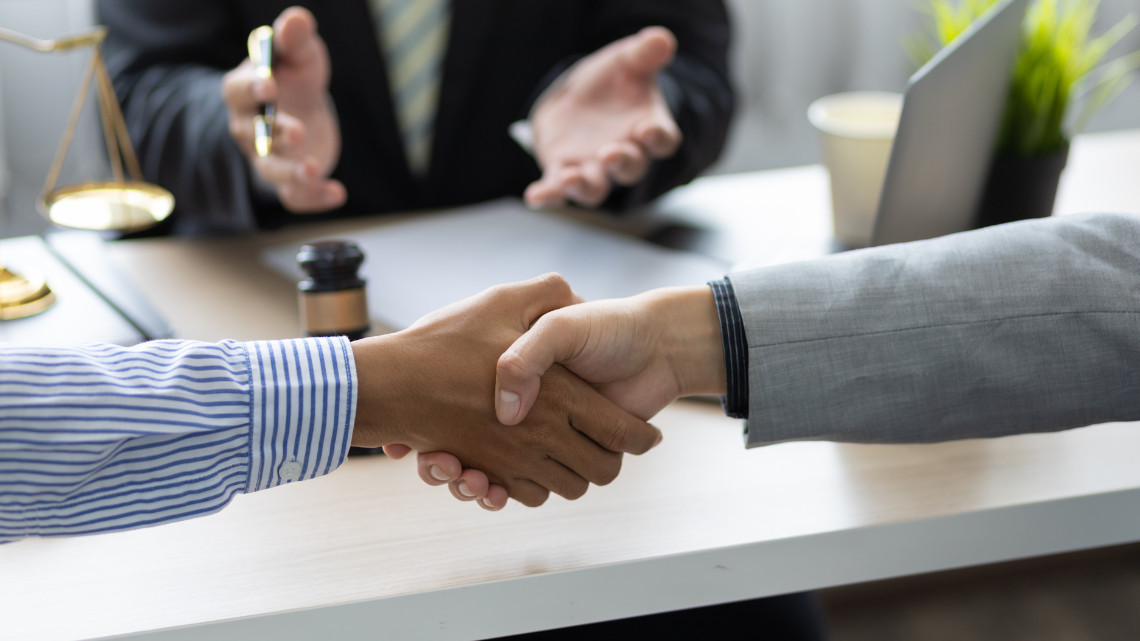 Handshake between two people in a professional setting with a gavel and scales of justice on the table, symbolizing mediation.