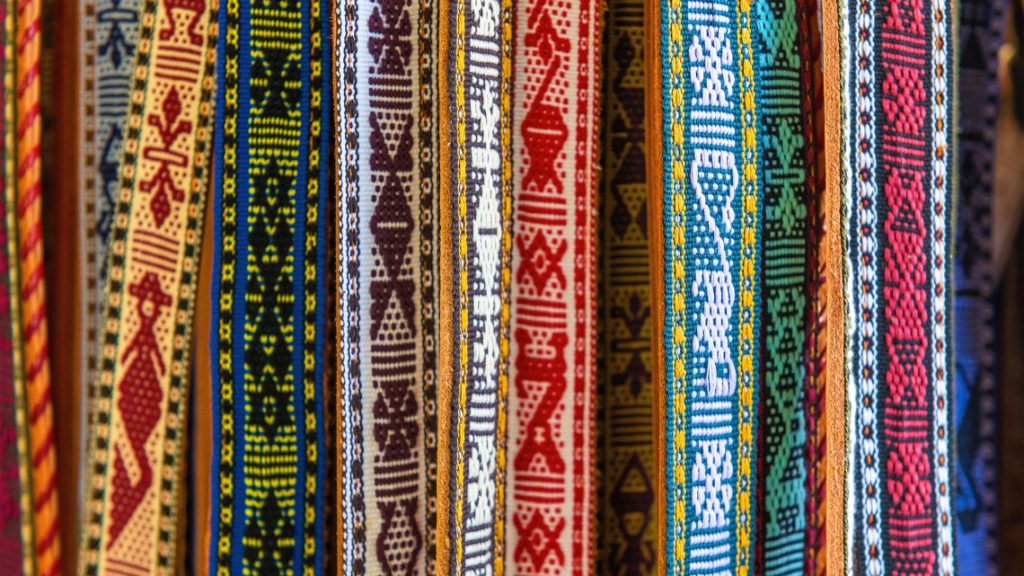 Colorful indigenous woven fabric ribbons with geometric patterns hanging vertically.