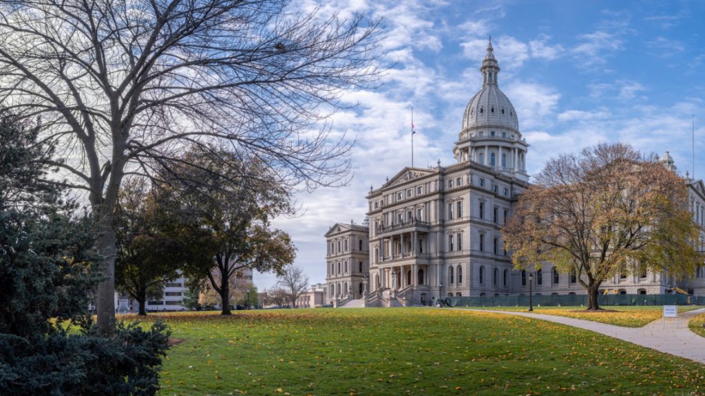 Michigan's capitol building surrounded by trees and a lawn with fallen leaves.